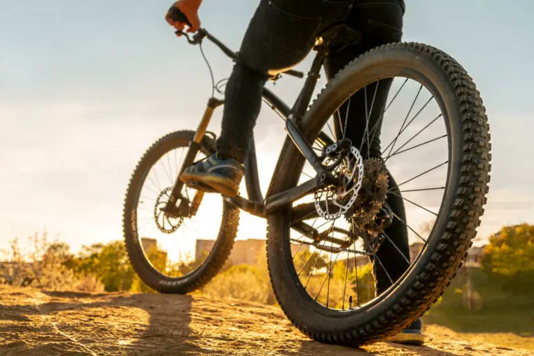 Man on mountain bike. Bicycle wheels close up image on sunset. Low angle view of cyclist riding mountain bike.