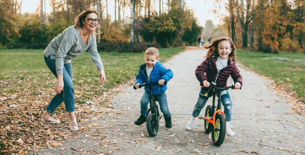 Lovely mother having a walk in the park with her children teaching them to ride the bike