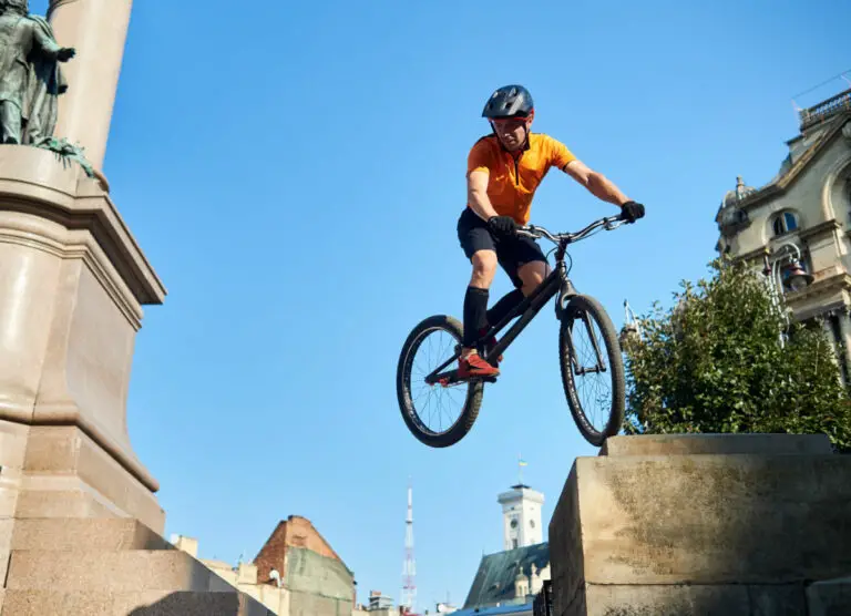 Young cyclist performing dangerous jumps on mountain bike on stairs of monument pedestal over blue sky, concept of extreme sport