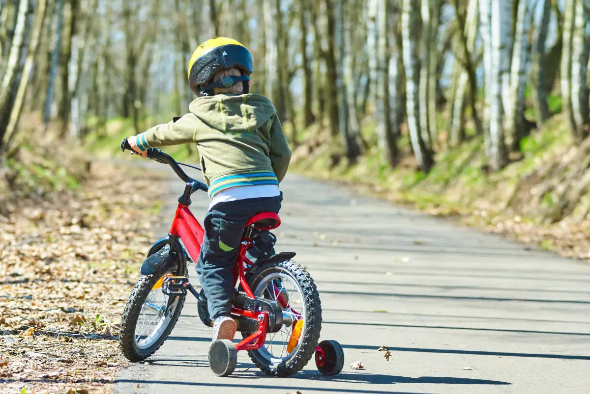 a boy riding a bike with training wheels in the park