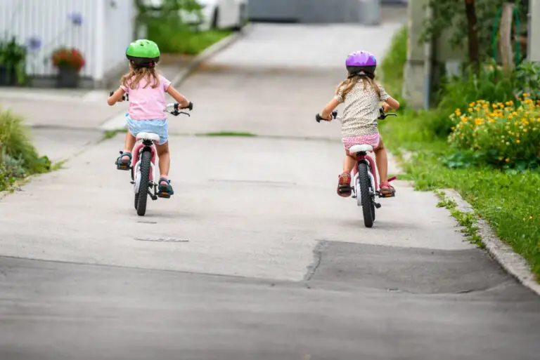Children learning to drive a bicycle on a driveway outside. Little girls riding bikes on asphalt road in the city wearing helmets as protective gear.